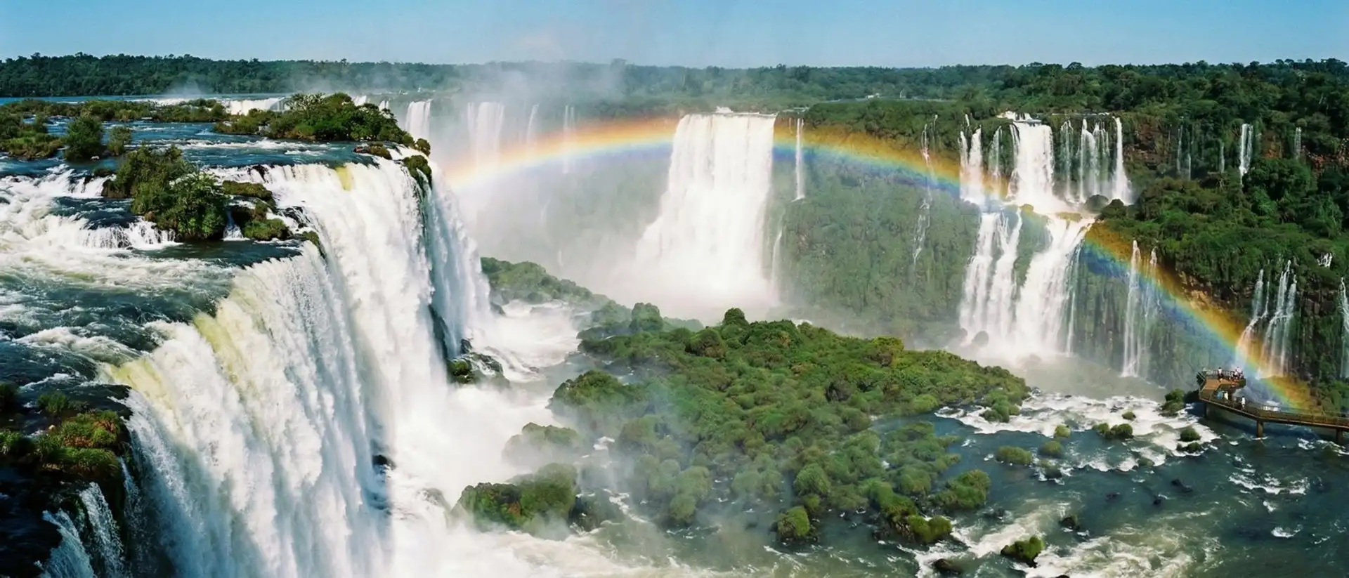 Wide panorama of Iguazu Falls with a full rainbow arching over the cascades